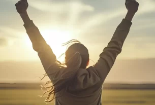 Imagem do devocional. Pessoa sorrindo com os braços erguidos ao céu durante o nascer do sol.