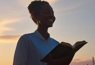 Imagem de uma pessoa sorrindo com a Bíblia aberta ao nascer do sol. Imagem do Devocional .