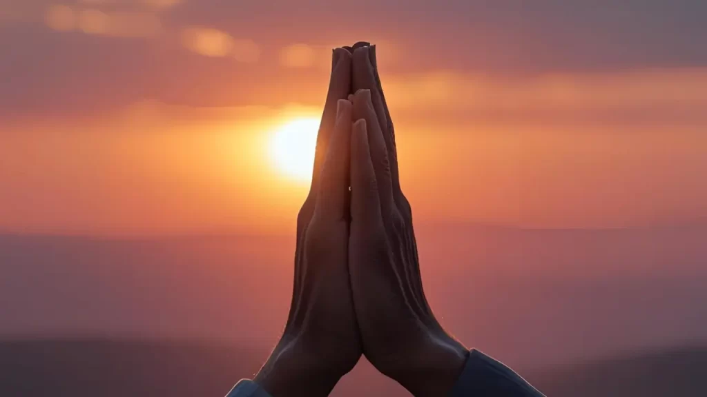 Mãos postas em oração ao pôr do sol, criando atmosfera de reflexão e entrega.
