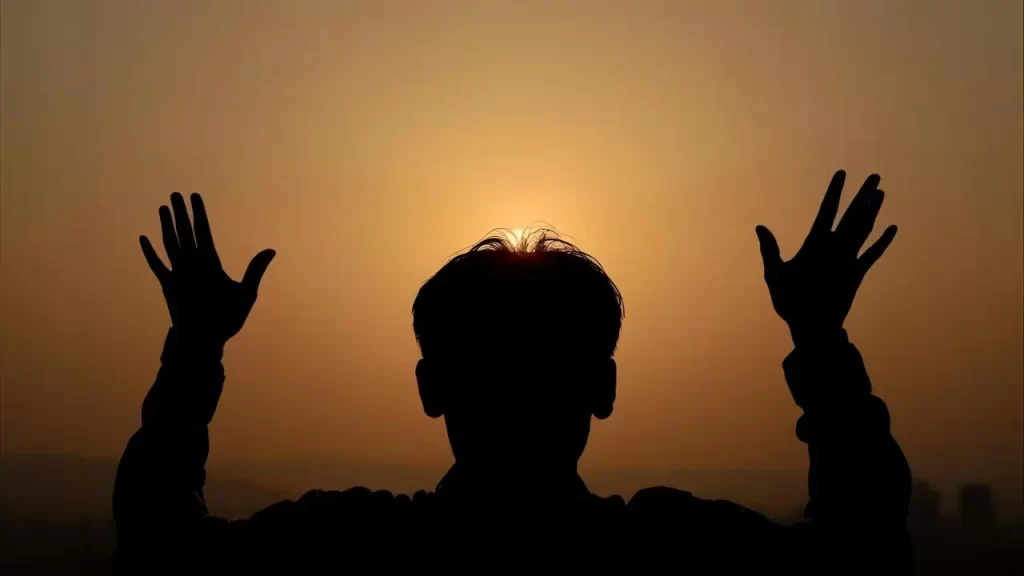 Silhueta de pessoa olhando o horizonte com as mãos levantadas.