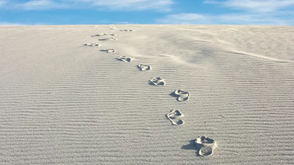 Marcas de pegadas na areia simbolizando segurança em Deus. 
