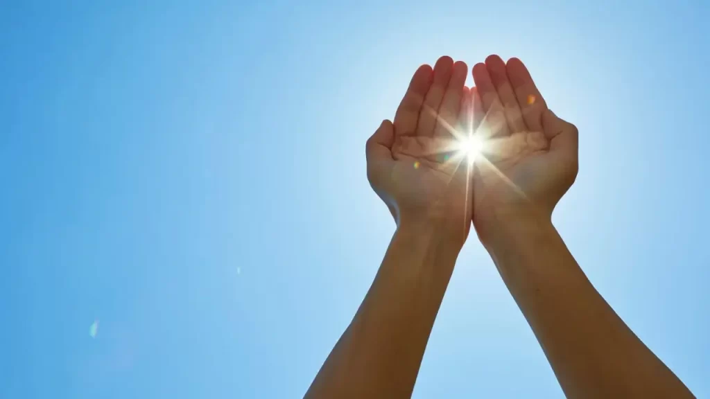 mãos estendidas ao céu com uma paisagem muito calma.