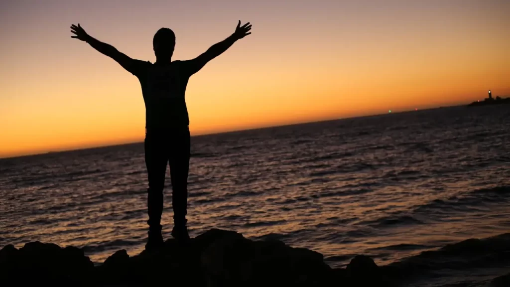 Pessoa com as mãos levantadas na praia em agradecimento a Deus por mais um dia. 