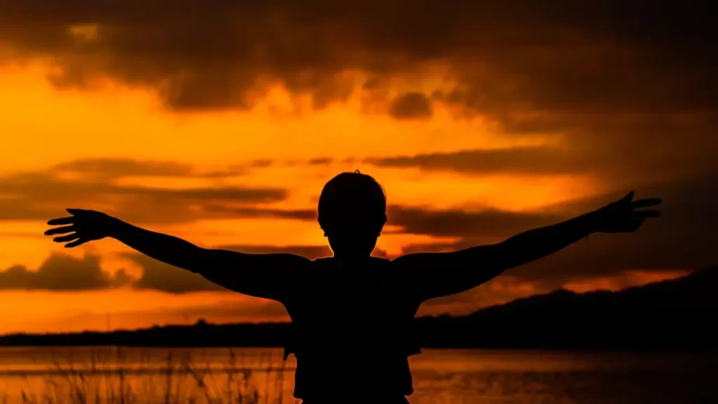 Silhueta de uma pessoa com braços erguidos em adoração. 